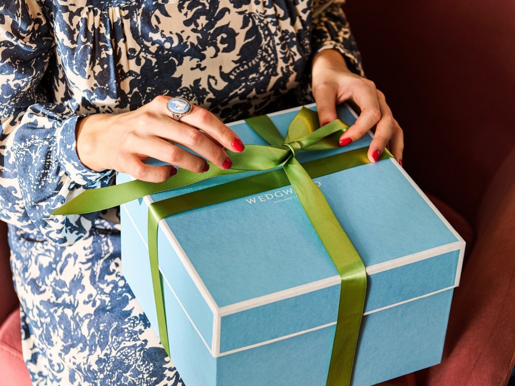 Woman in a blue floral dress wearing a blue Wedgwood ring, holding a Wedgwood gift box with green ribbon. Affiliated with SpookyMrsGreen.com pagan lifestyle blog.